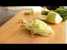 a cutting board with some cut up vegetables on it and someone in the background preparing food