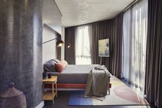 a bed sitting next to a window in a bedroom under a light on top of a wooden table