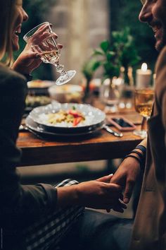 a man and woman sitting at a table with wine glasses in their hands by an empty plate on the table