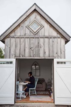 a woman sitting at a table in the back of a barn style shed with doors open