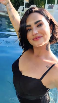 a woman in a black bathing suit standing next to a pool with her arm up