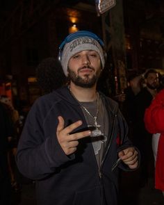 a man wearing a beanie and holding a cell phone in his hand while standing next to other people