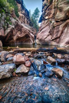 a man standing in the middle of a river surrounded by rocks and boulders with water running through it