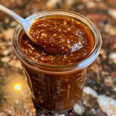 a spoon full of sauce sitting on top of a table next to a jar filled with something