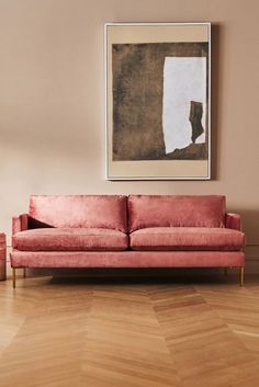 a living room with a pink couch and painting on the wall next to wooden flooring