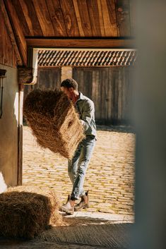 a man is holding hay in his hands while standing next to a building and looking at it