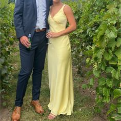 a man and woman standing next to each other in front of green plants, smiling at the camera