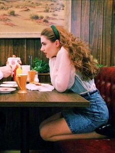 two people sitting at a table with plates and cups in front of them, talking