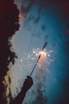 a person holding a sparkler in their hand with fireworks coming out of it and the sky behind them