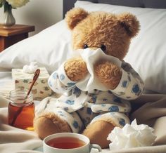 a teddy bear sitting on top of a bed next to a cup of tea and honey