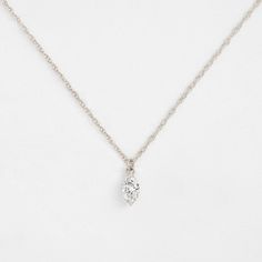 a necklace with a diamond on it sitting on top of a white surface, in the shape of a heart