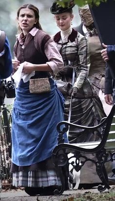 two women dressed in period clothing standing next to a bench