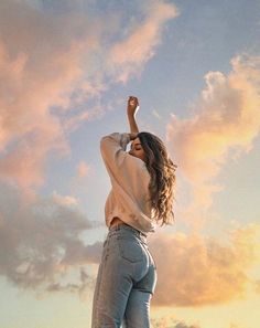 a woman standing on top of a hill with her arms in the air and looking up