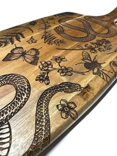 a wooden cutting board with an image of a snake on it's side and flowers in the background