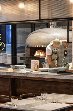 a man is cooking in a restaurant with an open fire place behind him and on the counter