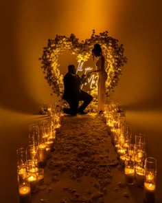 a newly married couple sitting in front of a heart - shaped archway with candles on the floor