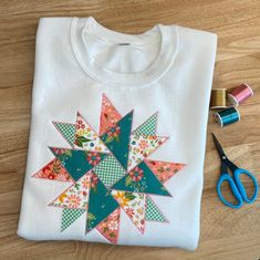 a white t - shirt with a colorful patchwork star on it next to scissors and spools of thread