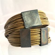 a close up of a bracelet on a white surface with a square metal object in the middle