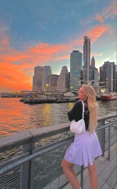 a woman is standing on a bridge looking at the water and buildings in the background