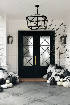 halloween decorations on the front porch of a house with black and white pumpkins, trees and lanterns