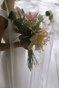 a woman holding a bouquet of flowers in her hand and wearing a white wedding dress