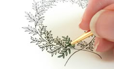 someone is drawing on paper with a pen and some leaves in the middle, while another hand holds a pencil