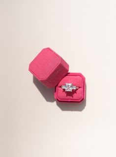 an engagement ring in a pink case on a white surface with a shadow from the top