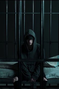 a man sitting on top of a bed in a jail cell with bars around him