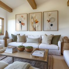 a living room filled with white furniture and paintings on the wall above it's coffee table