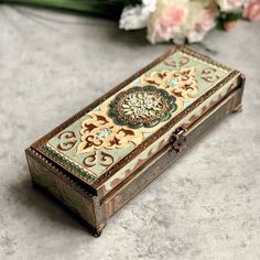 an ornate wooden box sitting on top of a table next to some pink and white flowers