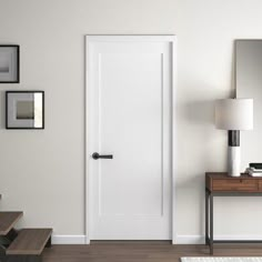 a white door in a room next to stairs and a table with a lamp on it