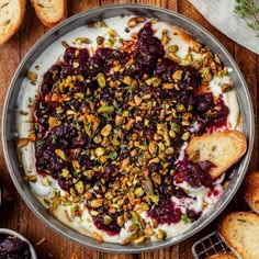 a pan filled with fruit and nuts on top of a wooden table next to bread