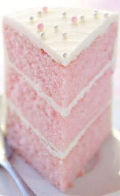 a piece of pink cake sitting on top of a white plate next to a fork