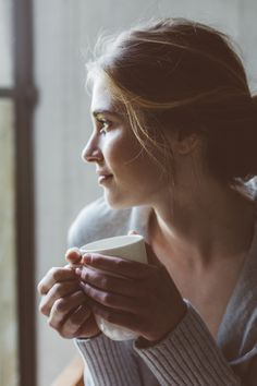 a woman is holding a cup in her hands and looking out the window at something outside