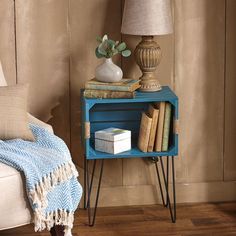 a blue table with books and a lamp on it next to a bed in a room