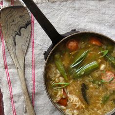 a pot filled with food next to a wooden spoon on top of a cloth covered table