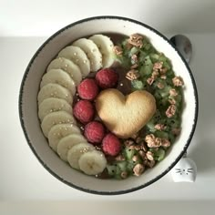 a bowl filled with bananas, raspberries, and other fruits next to a cookie in the shape of a heart