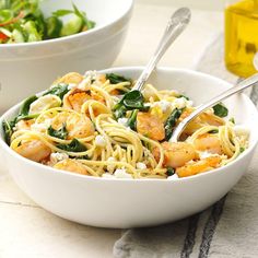 a bowl of pasta with shrimp and spinach on the side next to a salad