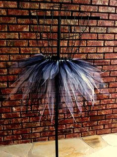 there is a blue and white tutu skirt hanging from a black metal stand in front of a brick wall