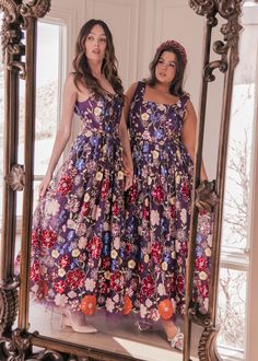 two women standing in front of a mirror wearing dresses with flowers on them and one is looking at her own reflection