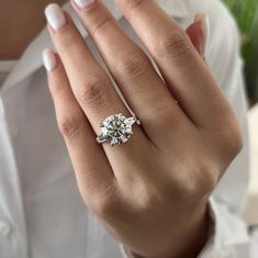 a woman's hand with a diamond ring on her left hand, and a white shirt in the background