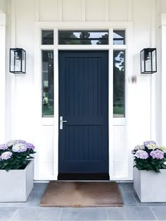 two white planters with purple flowers in front of a blue and white door on a house