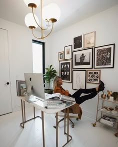 a woman sitting at a desk in front of a laptop computer with pictures on the wall behind her