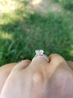 a close up of a person's hand with a ring on their finger and grass in the background