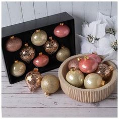 a wooden bowl filled with christmas ornaments next to a box of white and gold baubles