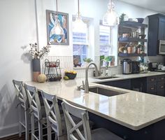 a kitchen with black cabinets and white counter tops, an island in the middle is surrounded by bar stools