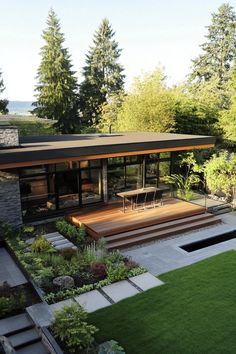 a modern house with an outdoor deck and grass area in the foreground, surrounded by trees