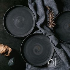 three black plates sitting on top of a table next to a plant and stoneware