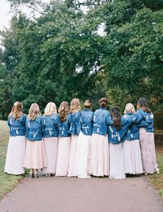 a group of women in long skirts and denim jackets are standing on a path with their backs to the camera