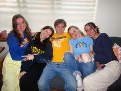 four young people sitting on a couch posing for the camera with their arms around each other